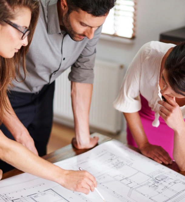 A group of three individuals studying a blueprint on a table, collaborating on design plans and ideas.